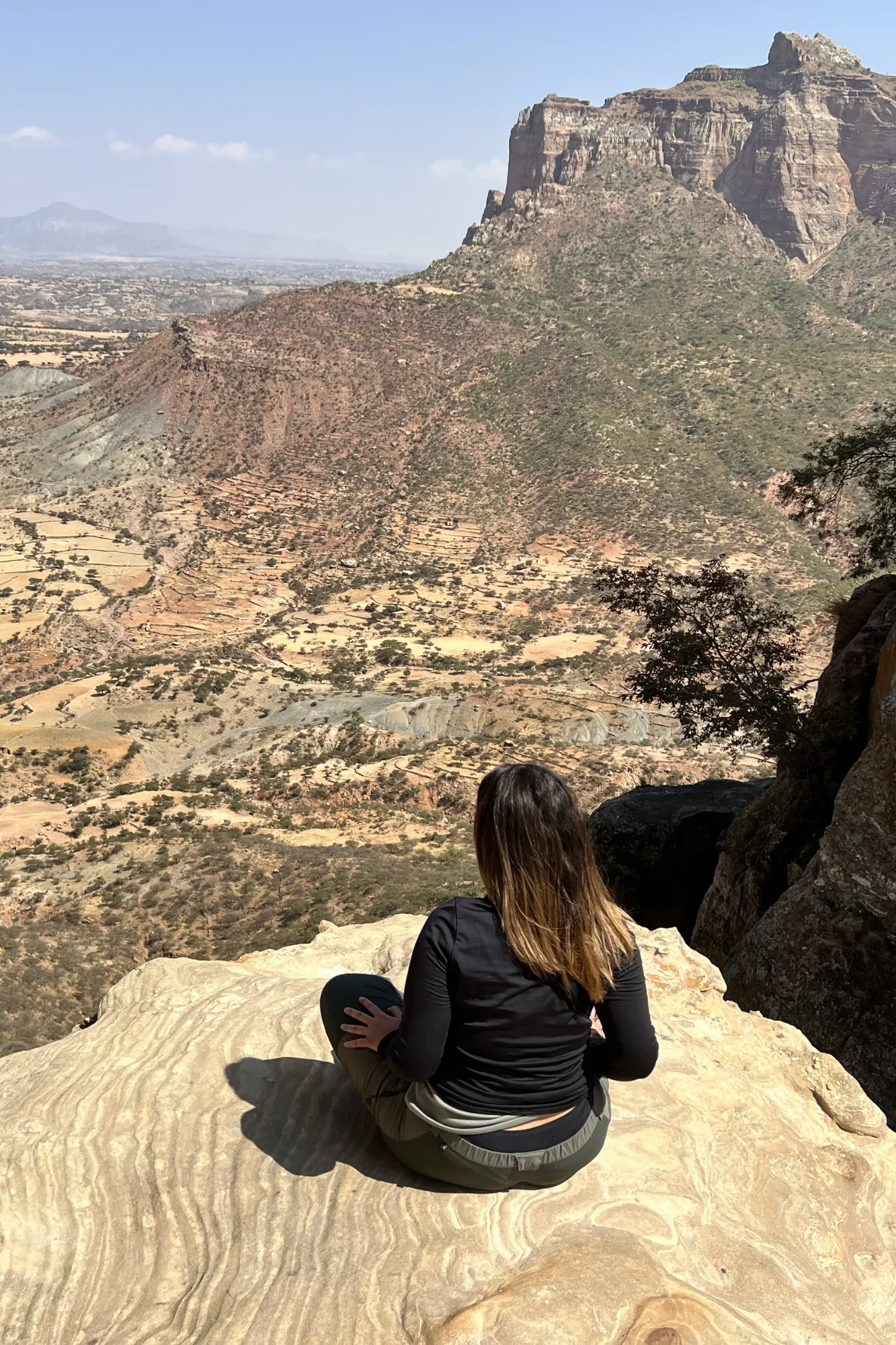 Viaggiatrice Yagiu seduta su uno sperone di roccia panoramico davanti alle montagne del Gheralta vicino alla chiesa di Abuna Yemata, in Etiopia.