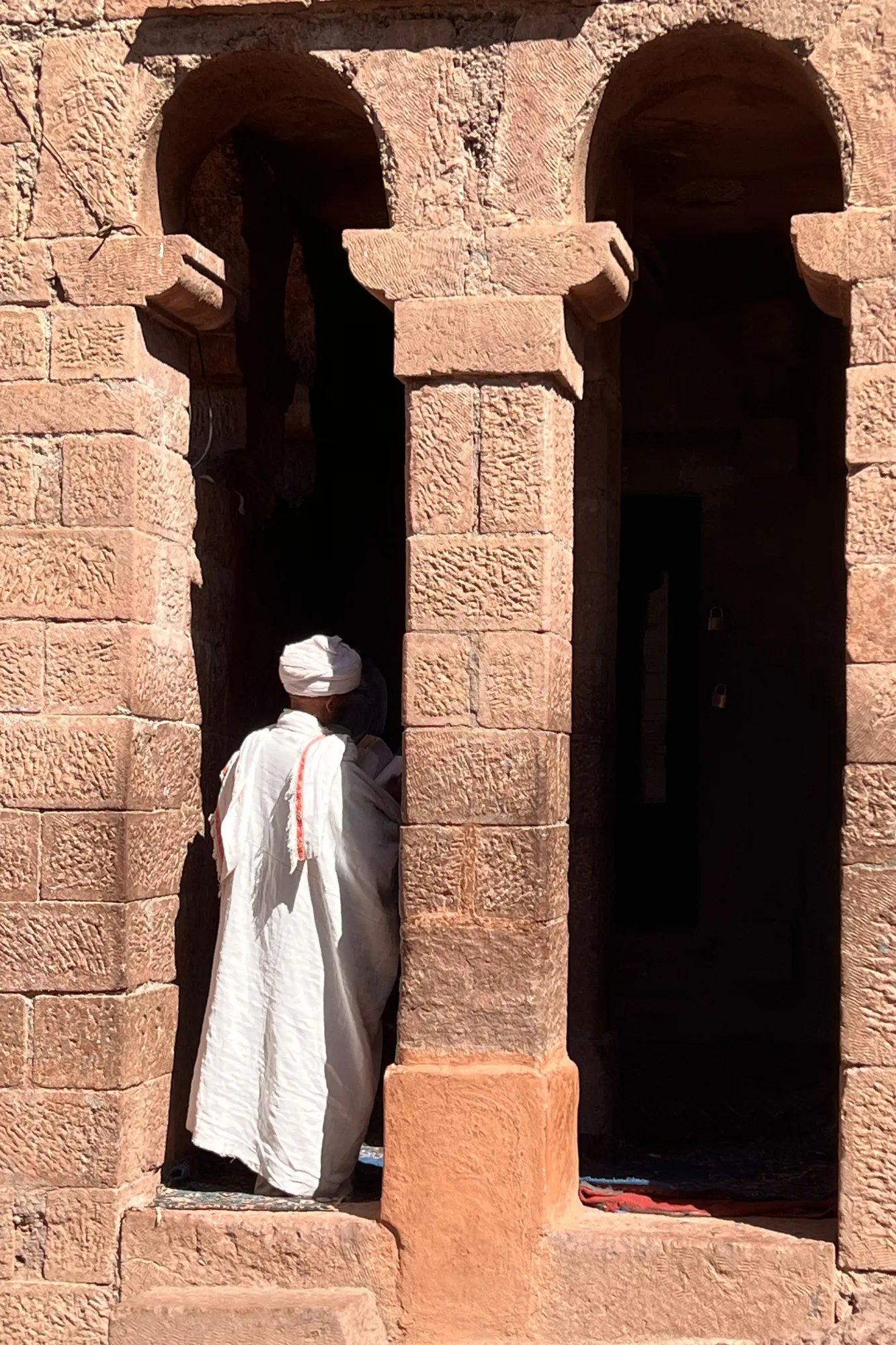 Un sacerdote ortodosso in abiti bianchi tradizionali tra gli archi scavati nella roccia di una chiesa a Lalibela, in Etiopia.