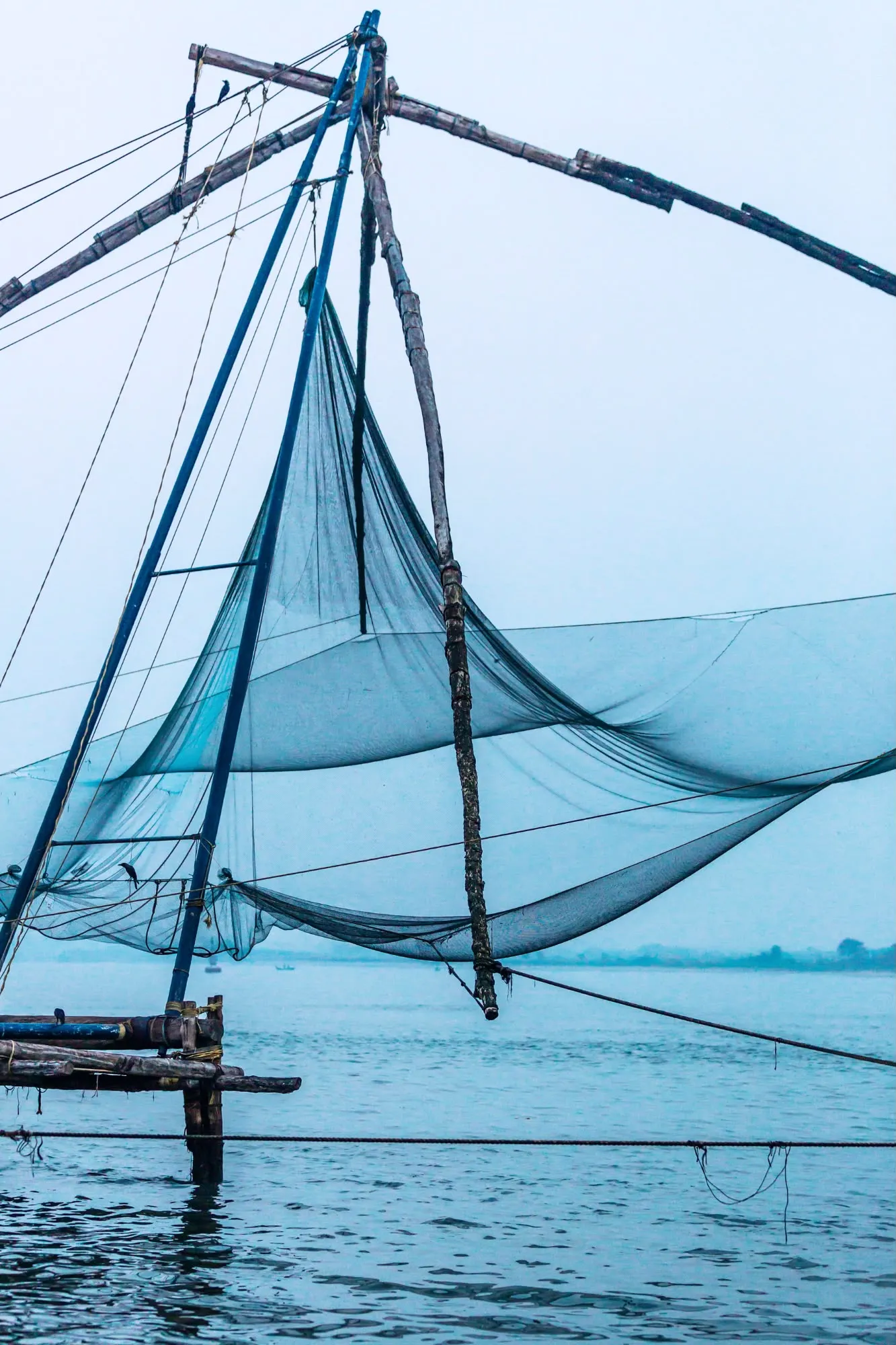Primo piano della rete da pesca cinese a Cochin sospesa sopra l'acqua azzurra in una giornata nebbiosa.