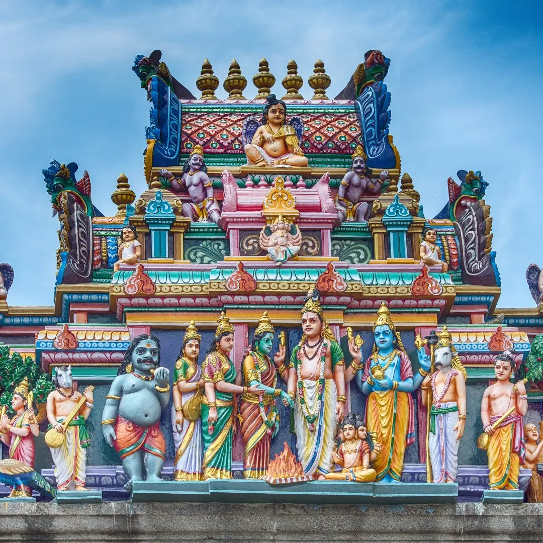 Facciata decorata di un tempio induista con numerose statue di divinità dipinte con colori vivaci sotto un cielo azzurro.