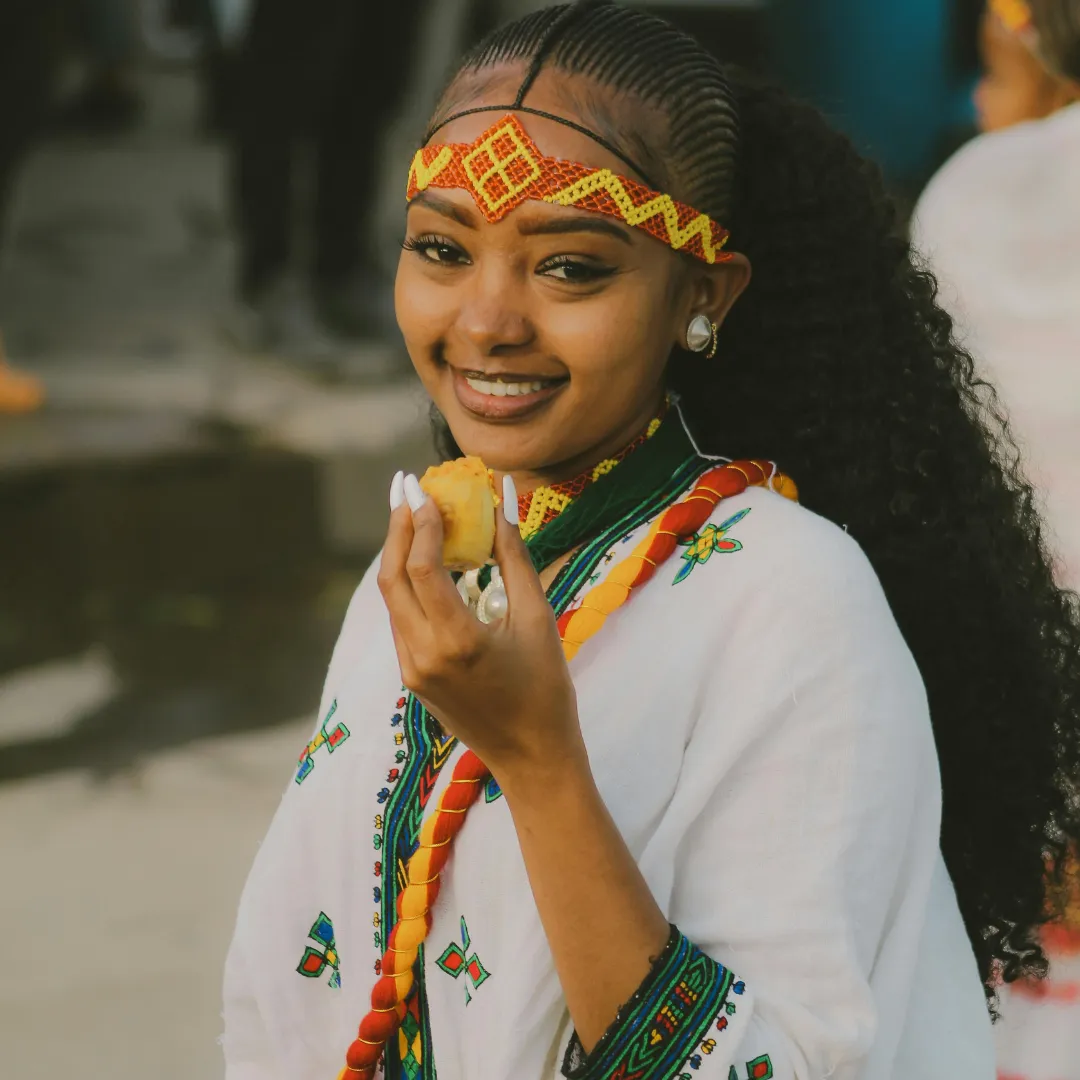 Ritratto di una donna etiope sorridente in abito tradizionale con pane dabo durante una cerimonia culturale in Etiopia.