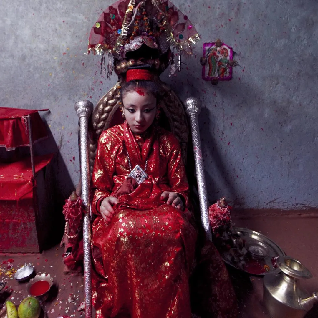 Bambina Khumari, ex dea vivente del Nepal, seduta in abiti cerimoniali rossi e oro su un trono decorato, durante un viaggio in Nepal.