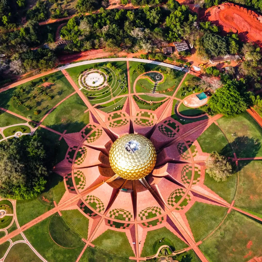Vista aerea dall'alto del Matrimandir ad Auroville, una grande cupola dorata circondata da giardini geometrici a raggiera.