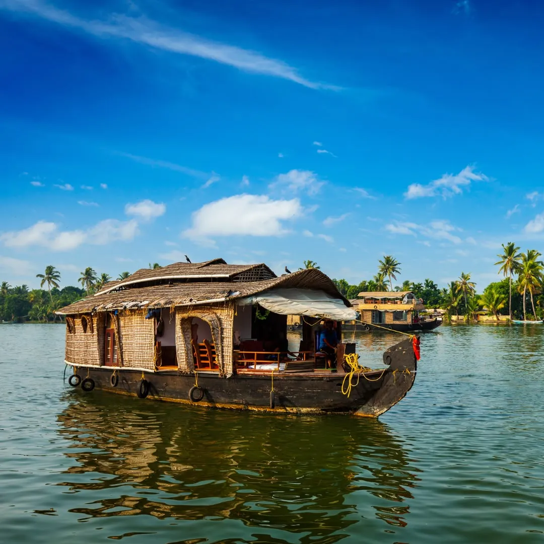 Una casa galleggiante indiana naviga sulle acque tranquille del Kerala sotto un cielo blu intenso e nuvole bianche.
