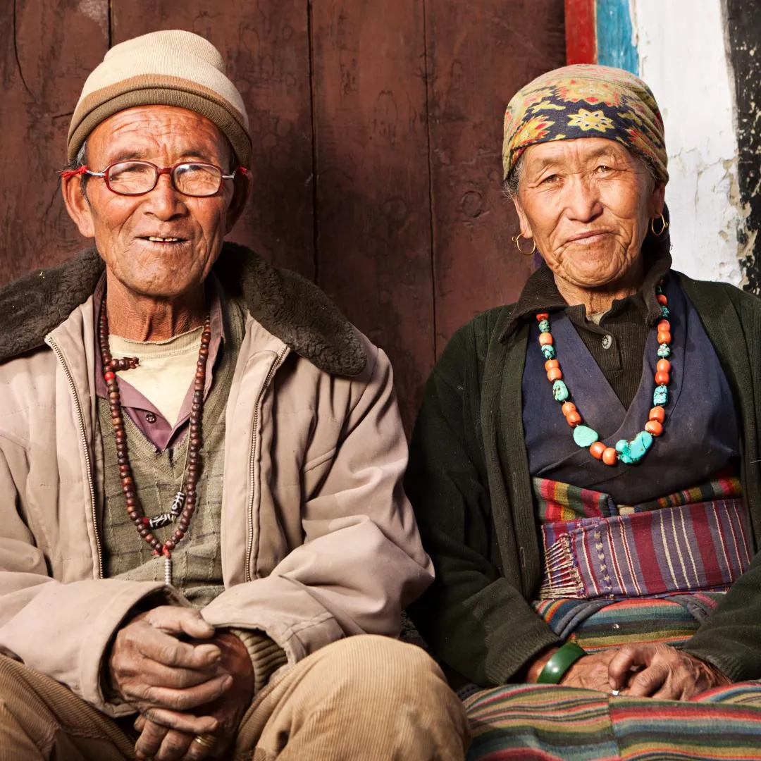 Coppia di anziani nepalesi in abiti tradizionali seduti all'aperto durante un trekking di gruppo in Nepal.