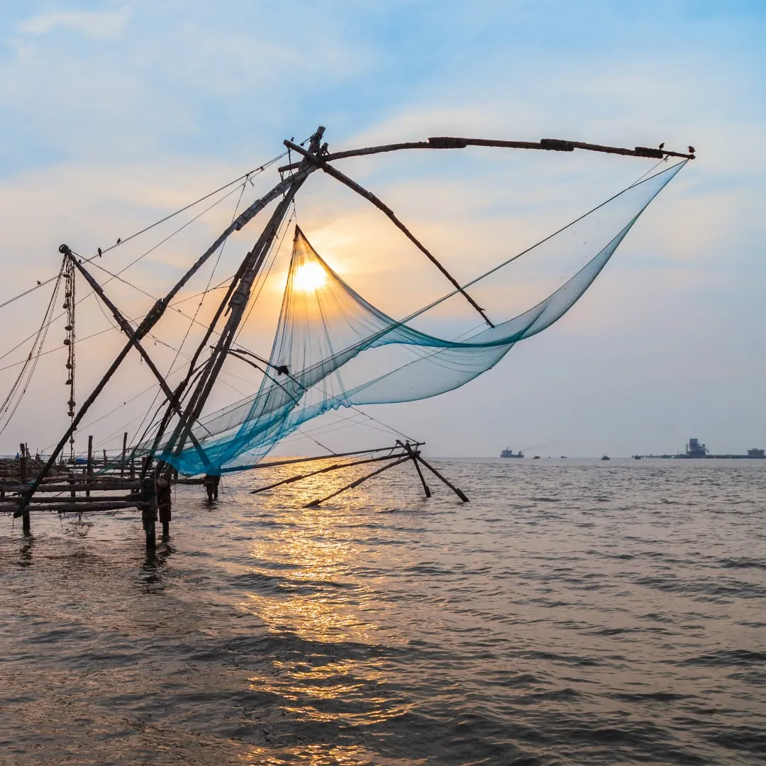 Una rete da pesca cinese a Cochin controluce con il sole splendente che si riflette sul mare calmo.