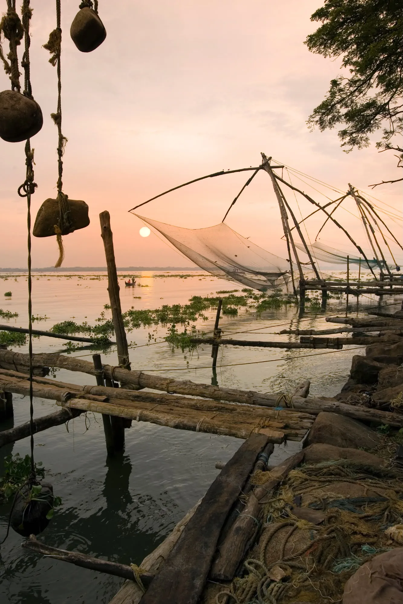 Reti da pesca cinesi in legno posizionate sull'acqua al tramonto con piccoli pontili in primo piano.