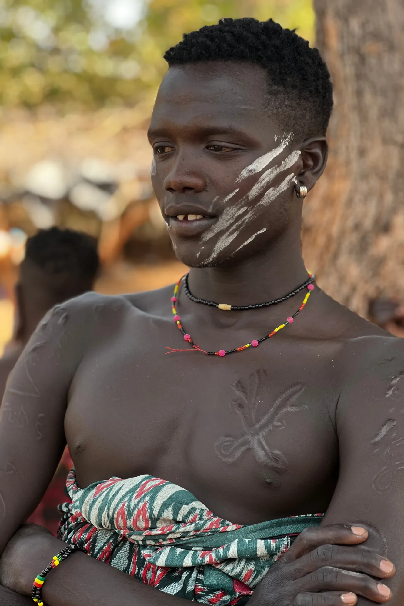 Primo piano di un giovane uomo della tribù Mursi con pitture facciali tradizionali in argilla e scarificazioni sul petto nella Valle dell'Omo in Etiopia.