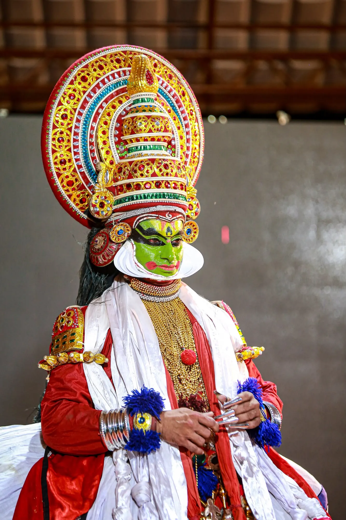 Attore di teatro Kathakali in Kerala con trucco facciale verde, costumi rossi tradizionali e un imponente copricapo decorato.
