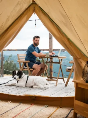 Digital nomad lavora al computer davanti a una tenda glamping in montagna con il suo cane