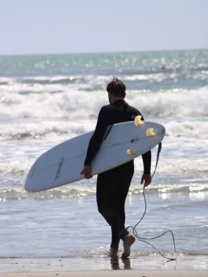 Surfista in muta nera cammina sulla riva del mare tenendo una tavola da surf bianca con pinne gialle