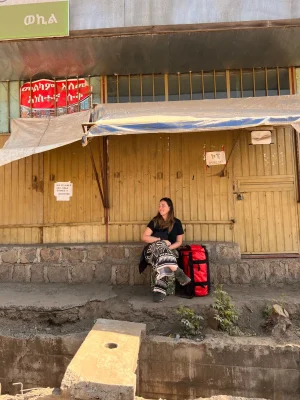 Ragazza seduta con zaino rosso north face da viaggio davanti a un negozio chiuso in un villaggio africano